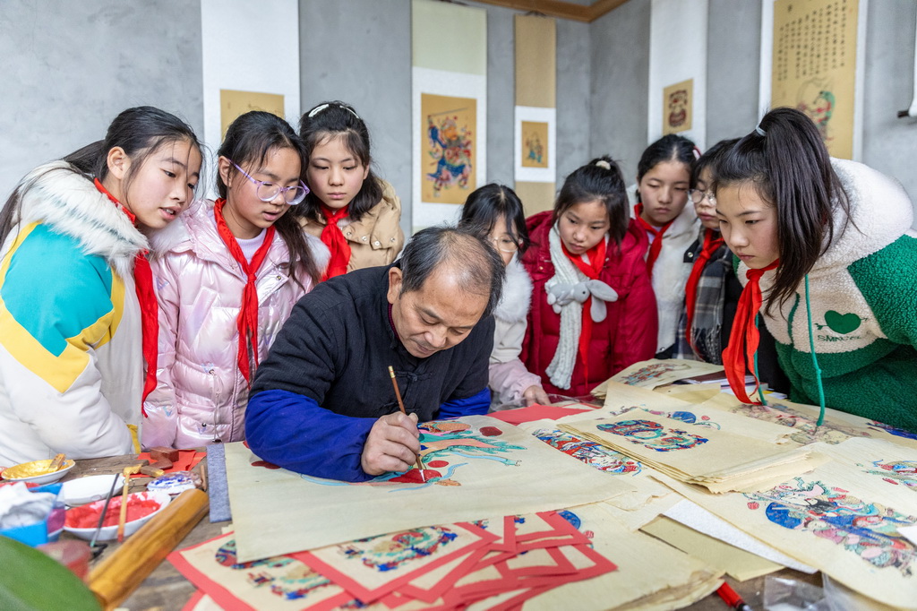 1月14日，在重慶市梁平區(qū)屏錦鎮(zhèn)，屏錦第三中心小學(xué)學(xué)生觀看梁平木版年畫國家級代表性傳承人徐家輝為年畫描色。